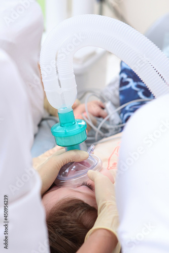 Little girl before surgery. The resuscitator holds an oxygen mask on the child's face. General anesthesia. Vertical photo. View from above. Life saving. Artificial lung ventilation apparatus.