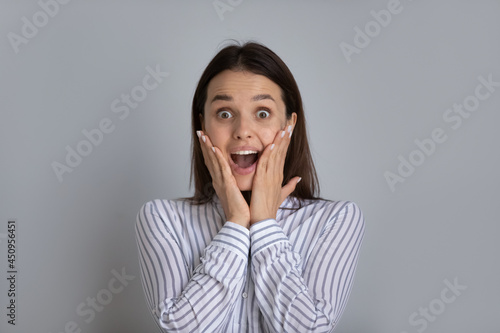 Portrait of happy excited millennial Caucasian woman isolated on grey studio background surprised by good sale offer or promotion discount or deal. Overjoyed young female shocked by unexpected news.