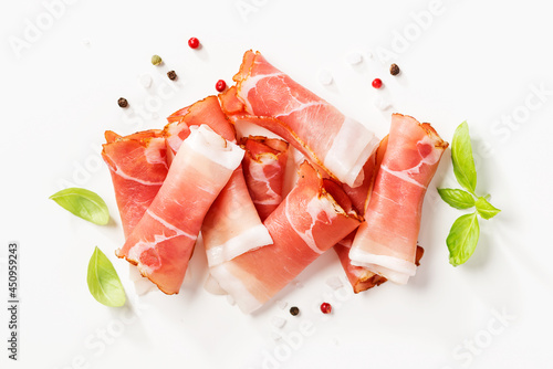Tasty prosciutto slices with basil leaves and spices on white background