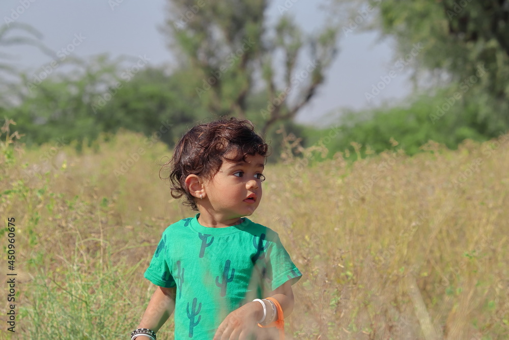 Beautiful little Indian boy posing outside in the nature and defocused background of plant outdoors