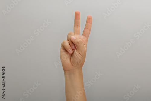 Teenage boy showing two fingers on light background, closeup