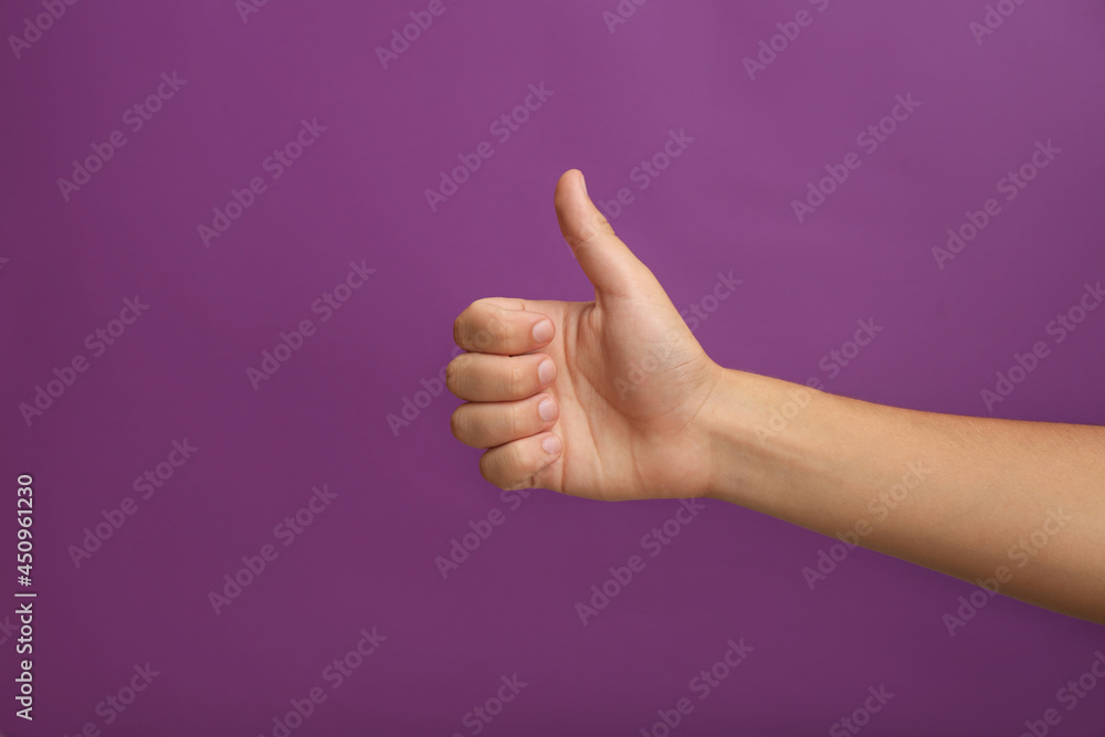 Teenage boy showing thumb up on purple background, closeup