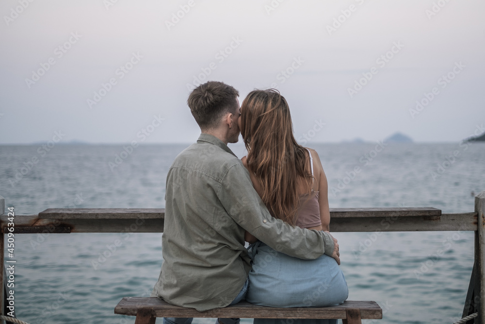 Back side view of the loving couple sitting on the bench near the sea. Looking at the ocean. Millennials. Romantic picture. High quality photo 