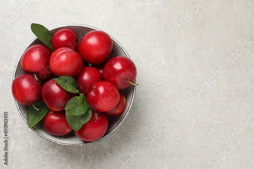 Delicious ripe cherry plums with leaves on light table, top view. Space for text