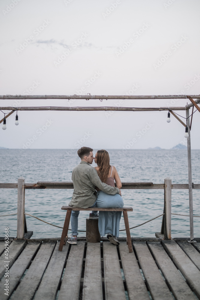 Lovely couple sitting on the wooden bench on the pier. Kissing and Cuddling. Millennials. Romantic picture. High quality photo 