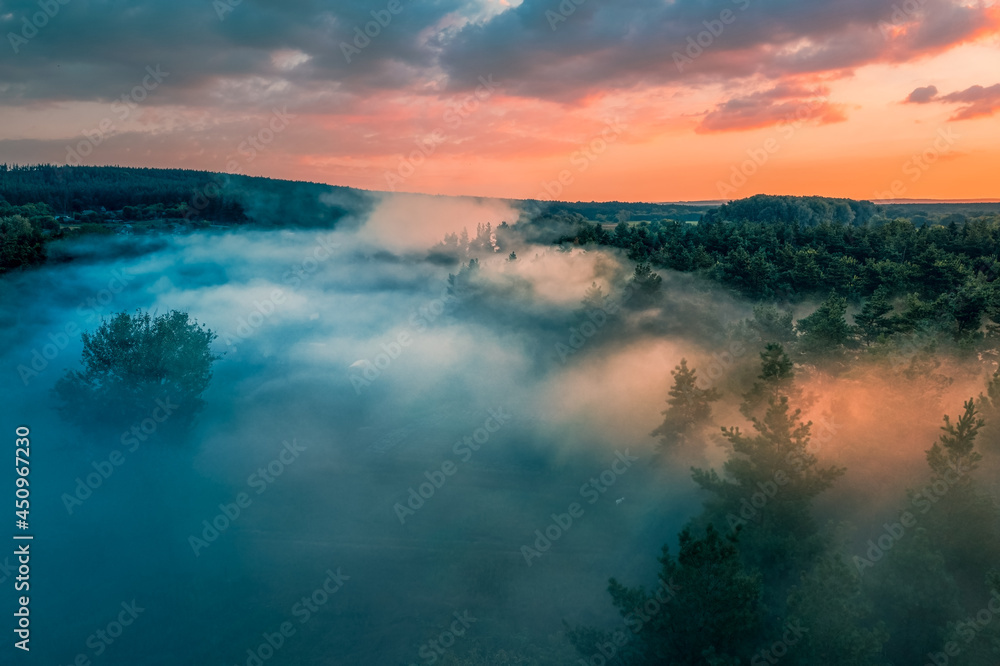 Misty dawn among trees at edge of forest: orange light of dawn sun against background of blue cold fog. Misty dawn among trees at edge of forest: orange light of dawn sun against background of blue cold fog.