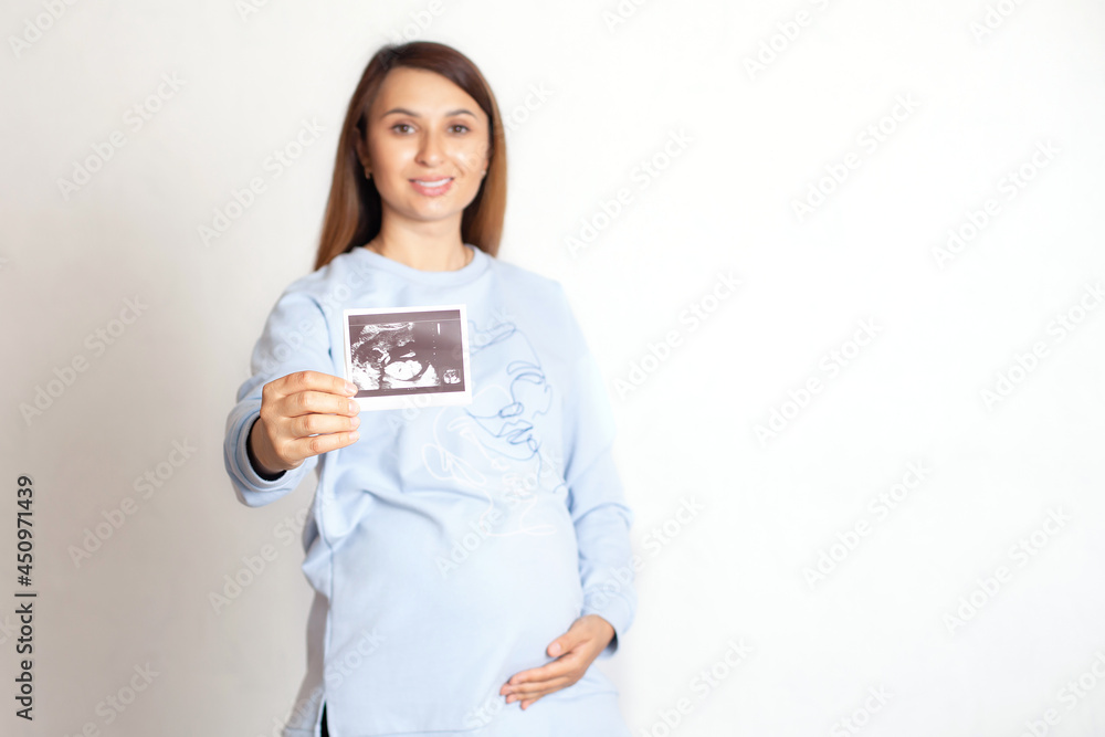 A beautiful pregnant woman with dark hair holds an ultrasound image of the child. screening. Pregnancy monitoring. White background, space for text A beautiful pregnant woman with dark hair holds an ultrasound image of the child. screening. Pregnancy monitoring. White background, space for text