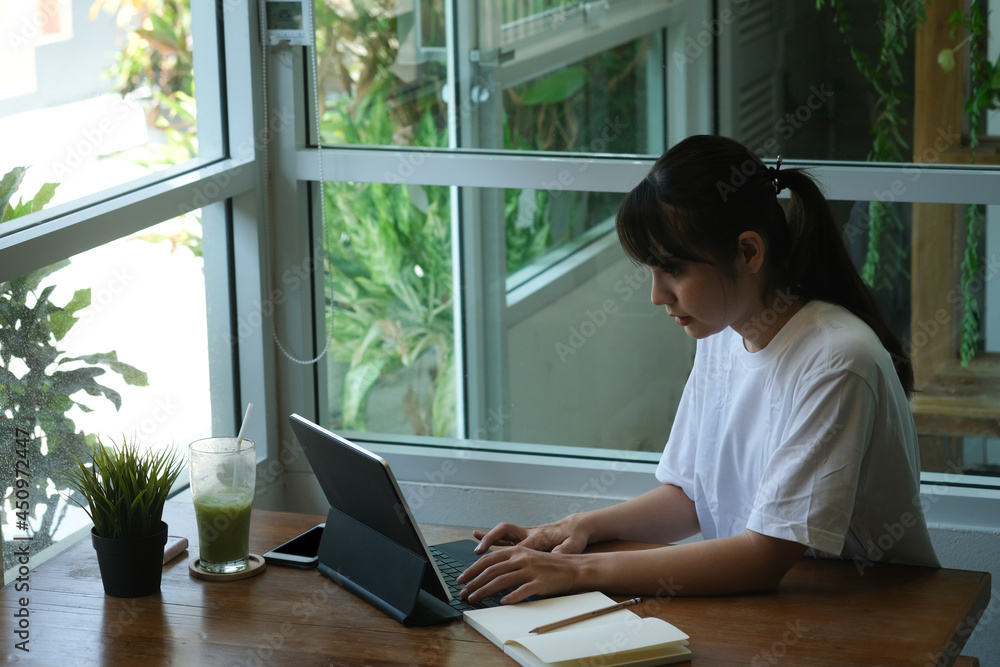 Young Asian student learning online with tablet and do her homework while sitting in cafe. Young Asian student learning online with tablet and do her homework while sitting in cafe.