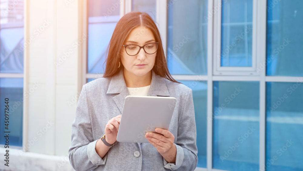 woman in a formal suit and glasses walks and looks at the tablet on the street. woman in a formal suit and glasses walks and looks at the tablet on the street.