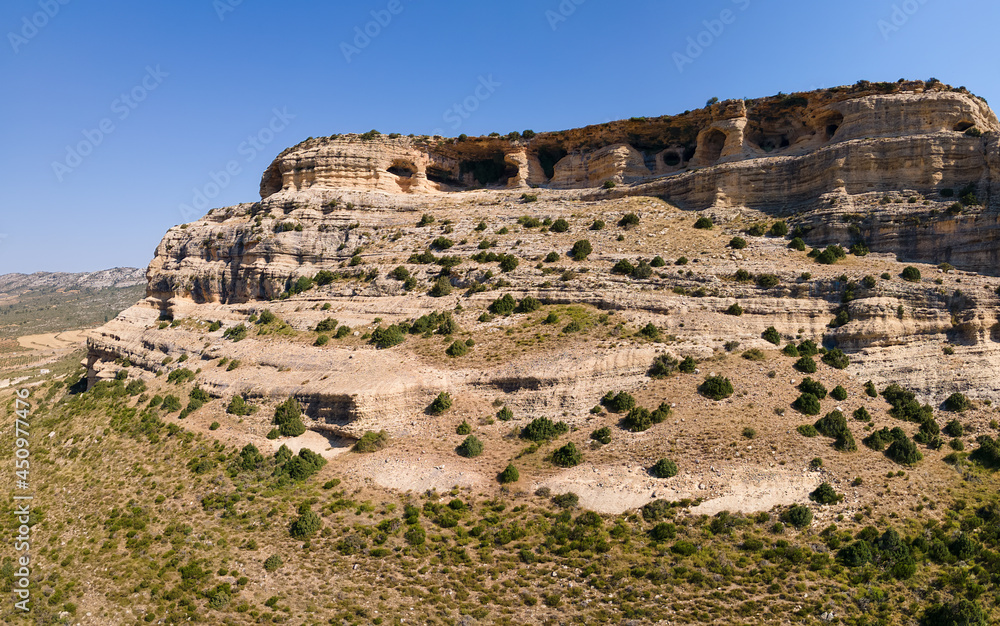 The mountain and caves of Zaen in the Spanish region of Murcia. It's an aerial photo taken with a drone. The sun is shining and the sky is blue.