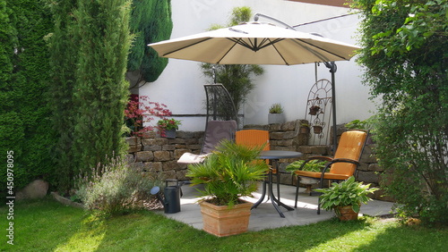 gemütliche Gartenterrasse mit Hängeschaukel und Sitzplatz umgeben von vielen Pflanzen und unter einem Sonnenschirm photo