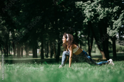 smiling woman in headphones doing stretching before jogging outdoor.