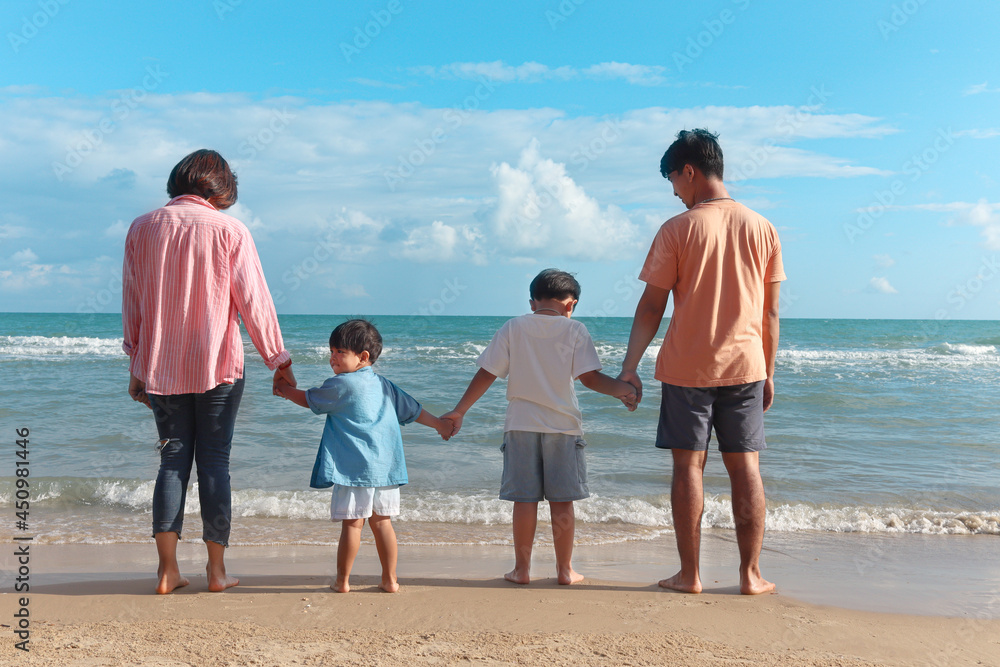 Happy family four spend time and have fun together on summer holiday vacation, cheerful parents children hold hands from behind on tropical sea beach, resting and relaxing weekend on beach. Happy family four spend time and have fun together on summer holiday vacation, cheerful parents children hold hands from behind on tropical sea beach, resting and relaxing weekend on beach.