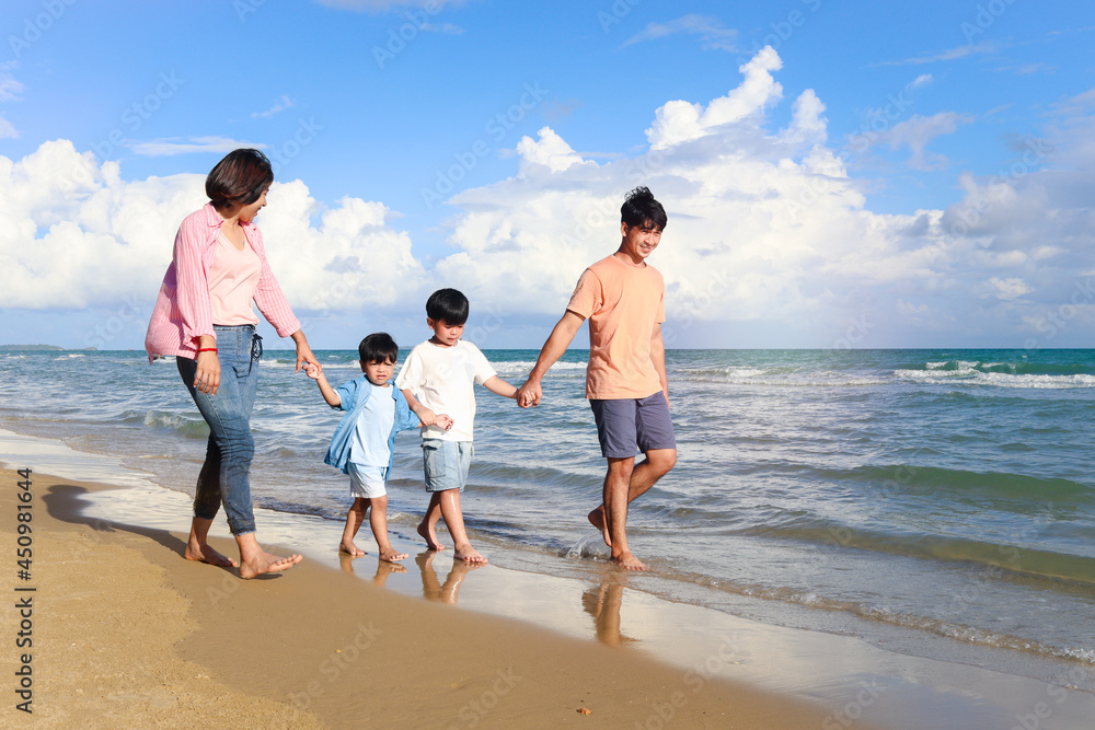 Happy family of four spend time together on summer holiday vacation, parents and children holding hand and walking along tropical sea beach, mother father and kids resting and relaxing on weekend