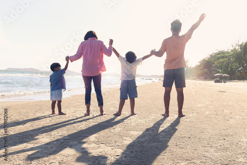 Happy family of four spend time and have fun together on summer holiday vacation, cheerful parents children hold and raise hand up from behind on tropical sea sand beach, resting and relaxing weekend