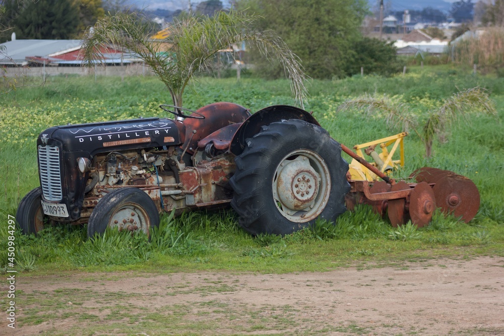 A tractor parked in the grass with cultivating machine attached to the back for farming purposes. A tractor parked in the grass with cultivating machine attached to the back for farming purposes.