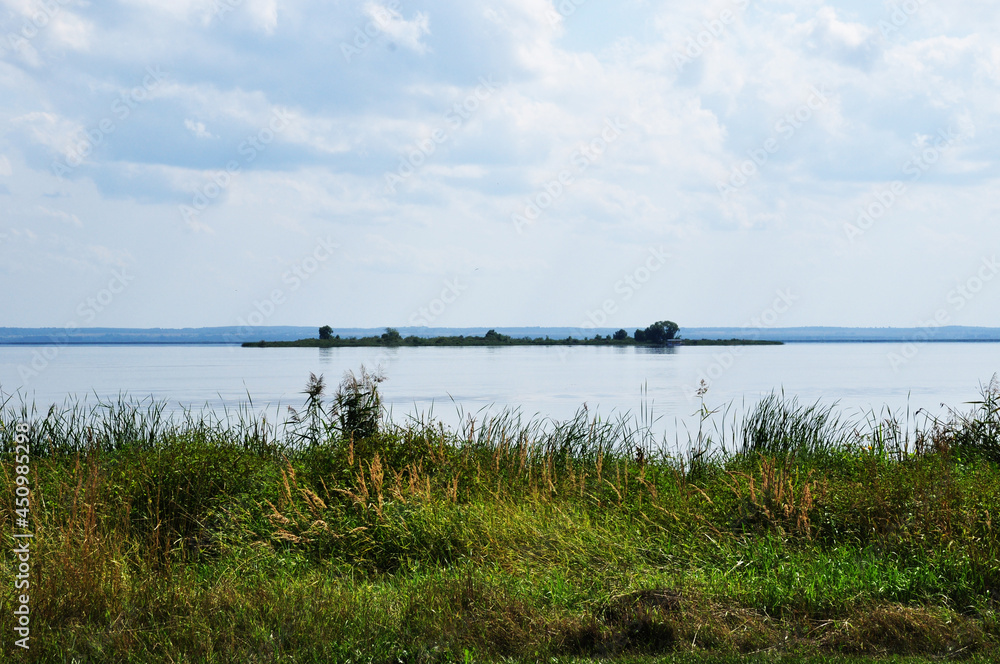 Panoramic view of Lake Nero. The coast is overgrown with tall grass and an islet on the shore of the lake. Summer.