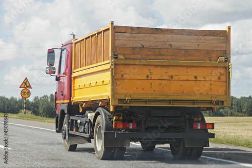 Transportation of bulk harvest, yellow dump truck drive on a European countryside highway asphalted road on field and blue sky background at autumn day