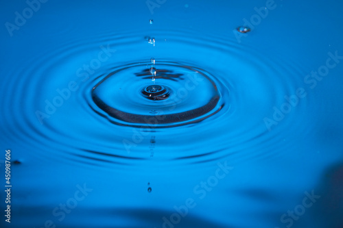 Beautiful view of drops making circles on blue water surface isolated on blue background.