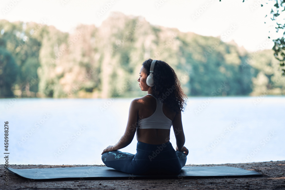 sporty woman wearing headphones meditating in the lotus position