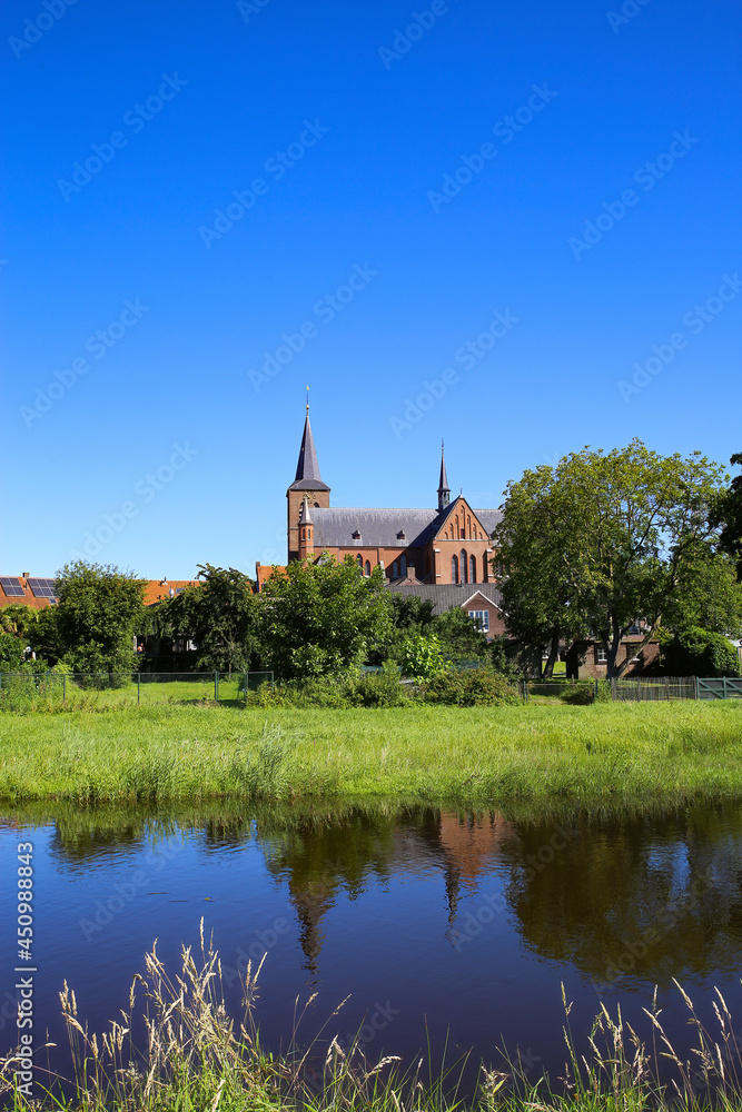 View over river and green pasture on small dutch idyllic village with medieval old church against blue cloudless summer sky - Neer (Limburg), Netherlands