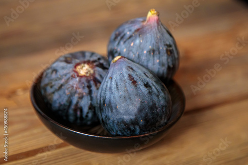 Fresh purple figs in a bowl on a wooden background from old boards. Raw exotic figs. Low key