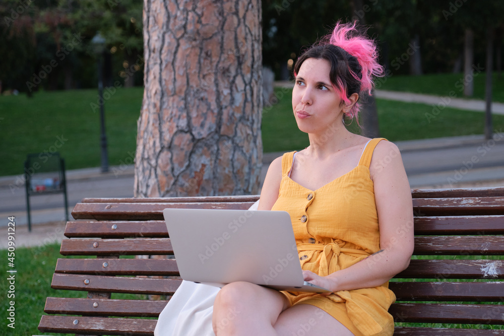 Young caucasian woman with pink hair thinking while working on a laptop. Young caucasian woman with pink hair thinking while working on a laptop.
