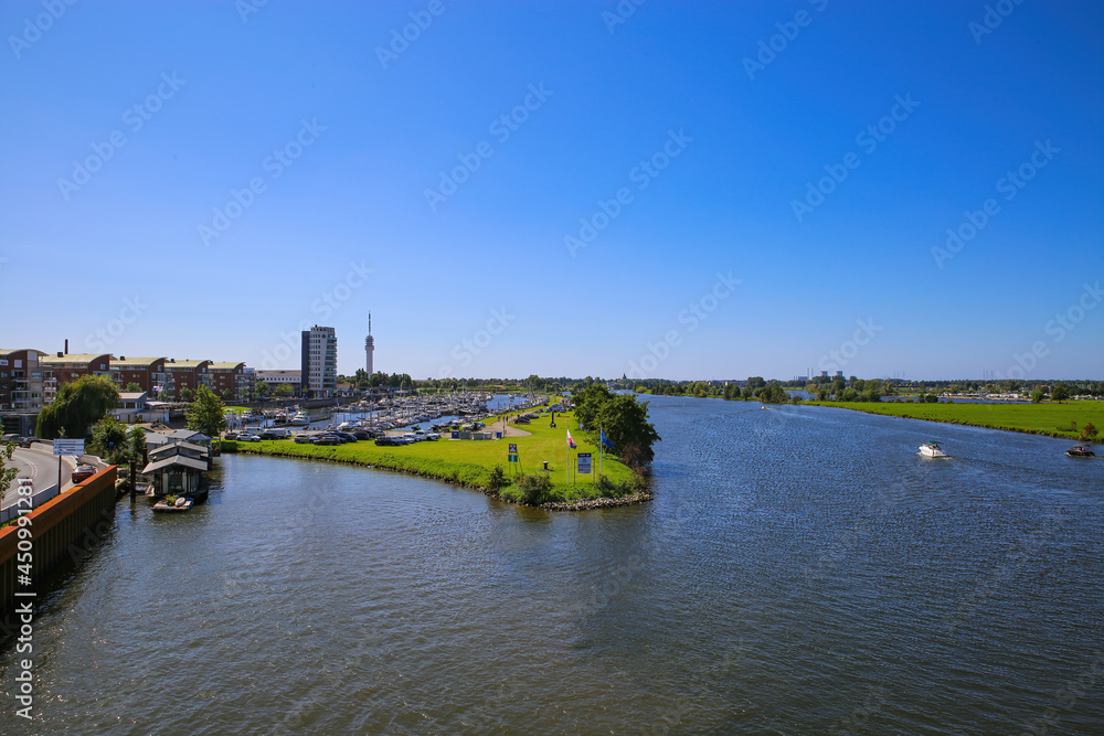 Fototapeta premium Roermond (Marina Oolderhuske), Netherlands - July 9. 2021: View on harbor with motor boats and sail yachts against blue summer sky, citiyscape and river maas background