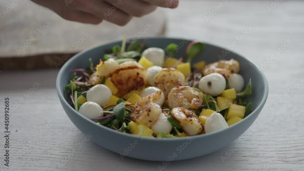 Man seasoning salad with shrimps, mango, mozzarella and micro greens Man seasoning salad with shrimps, mango, mozzarella and micro greens