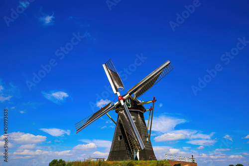 Beesel, Netherlands - July 9. 2021: View on isolated typical dutch windmill (Molen de grauwe beer) in rural landscape against deep blue summer sky with cumulus clouds