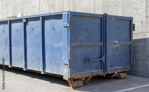 Metal durable blue industrial trash bin for outdoor trash at construction site. Large waste basket for household or industrial waste. A pile of waste.