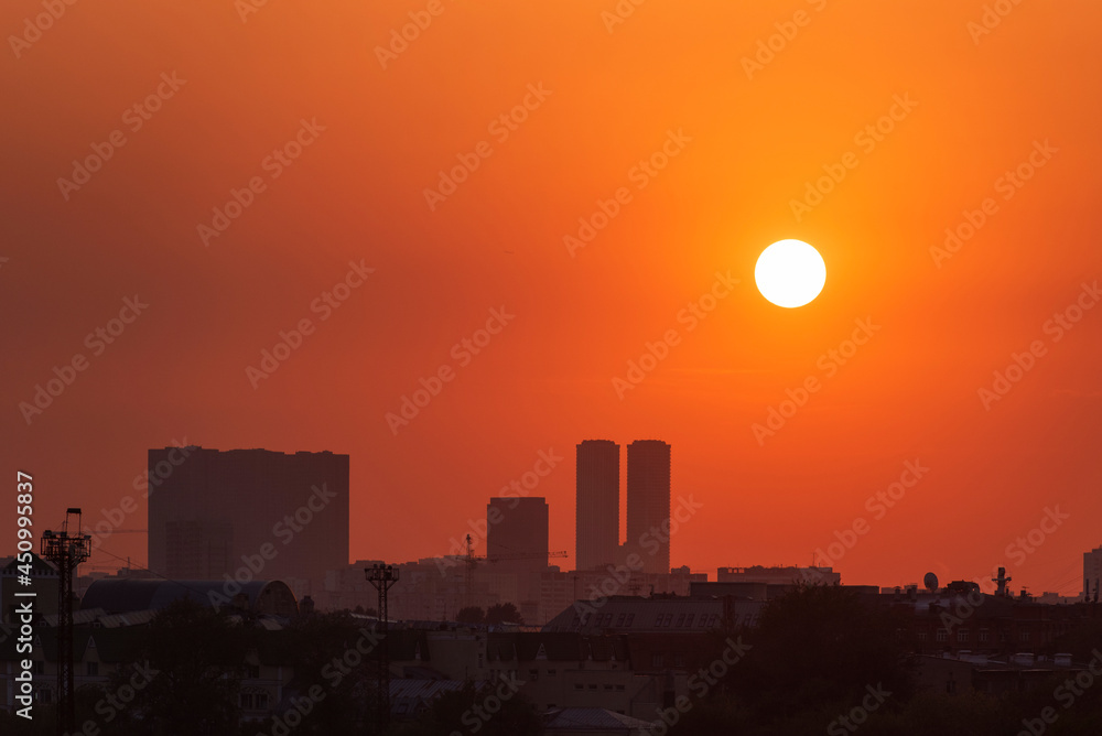 Urban skyline during orange sunset. Cityscape and round sun, summer sunset.