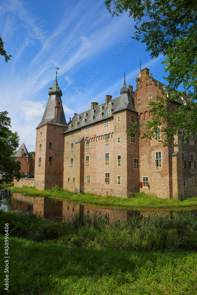 View beyond green trees on dutch water castle from 14th century against blue summer sky