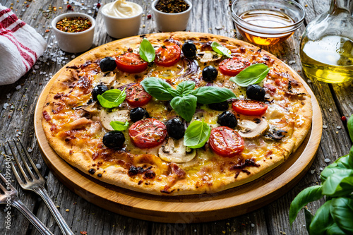 Circle pizza with mozzarella, white mushrooms, salami and tomatoes on wooden table 
