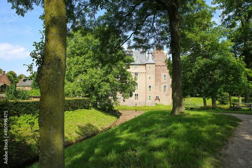 View beyond green trees on dutch water castle from 14th century against blue summer sky