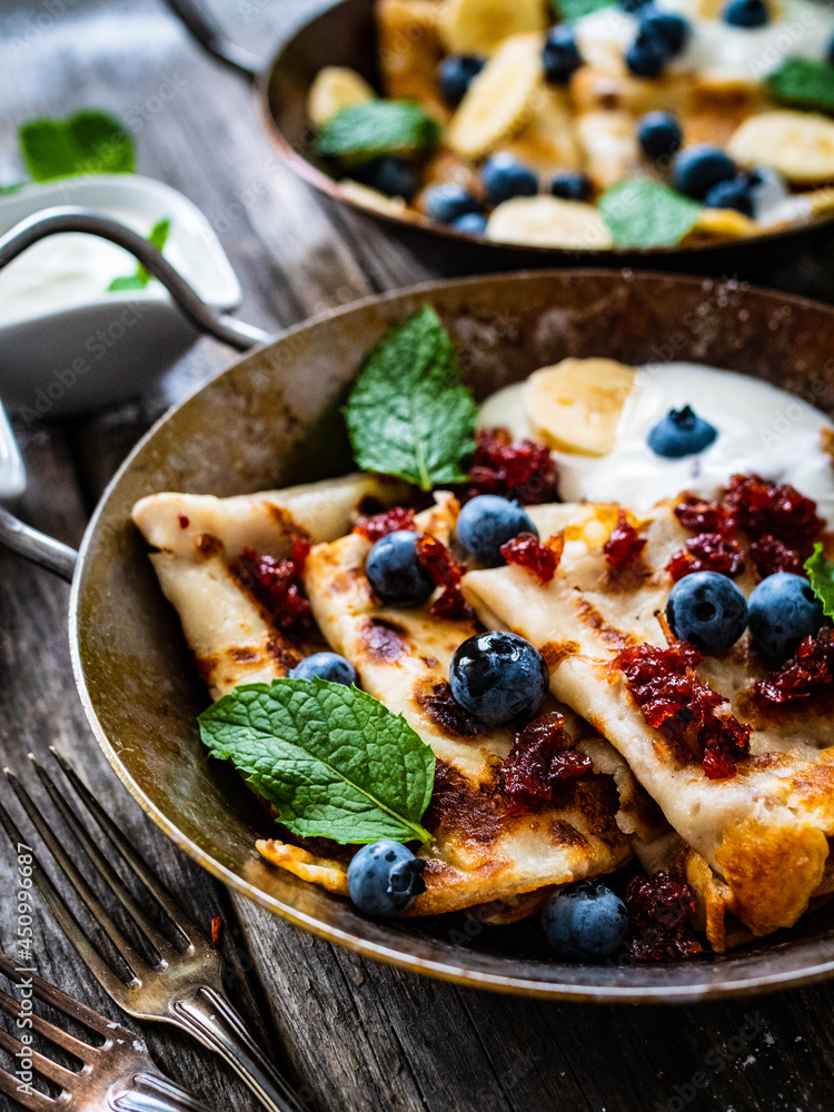 Sweet crepes with strawberries jam and blueberries in pan on wooden table
