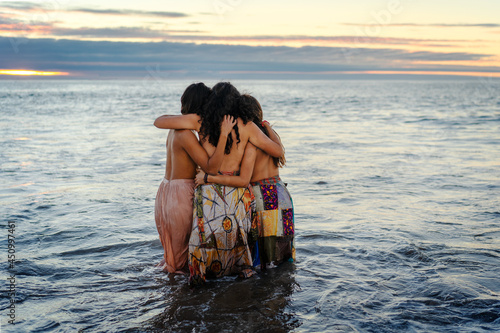 Tableau sur toile three young latin women hug each other in the water at sunset, showing friendshi