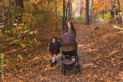 Mother and her little daughter and a baby in pram on walk in autumn wood
