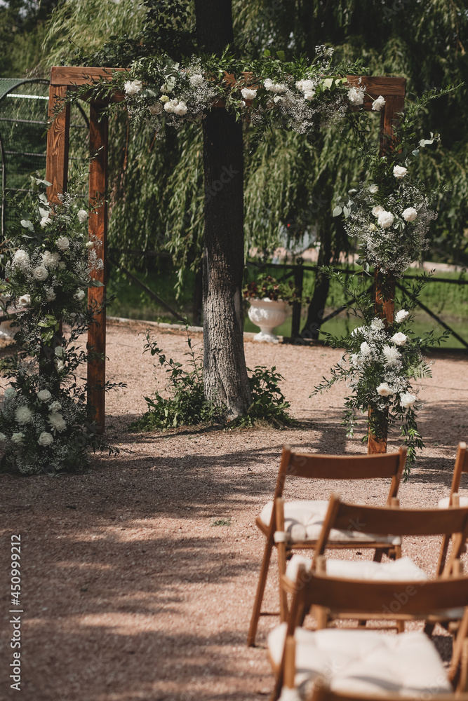 Wedding arch on boho style with white flowers in park.