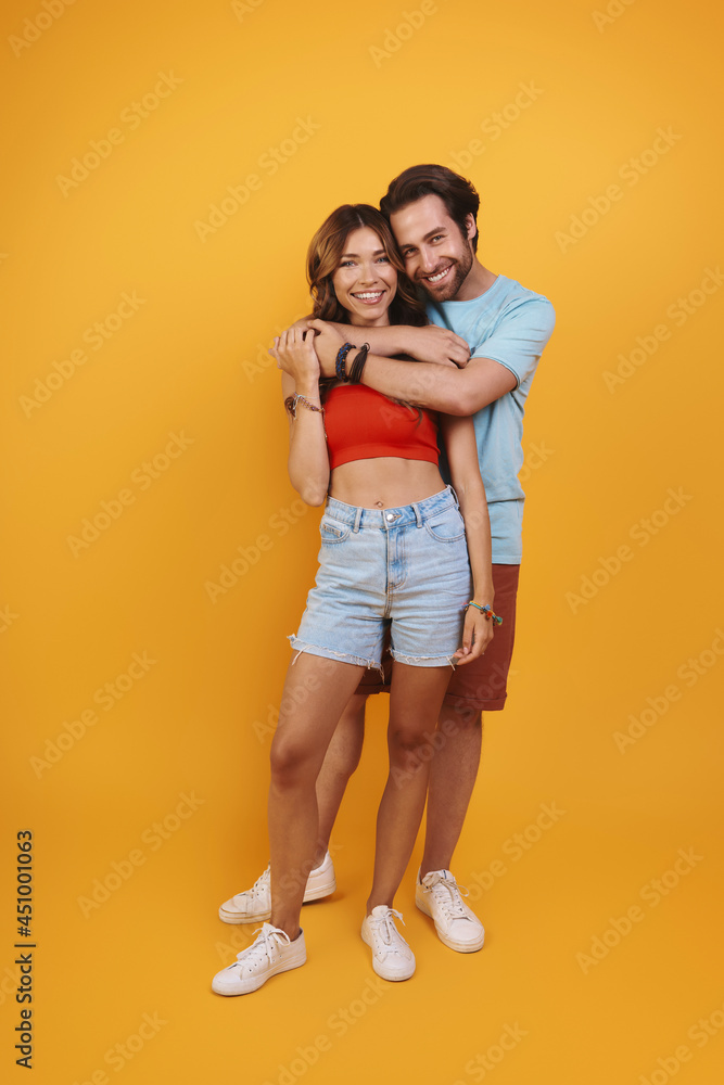 Full length of beautiful young couple embracing while standing against yellow background Full length of beautiful young couple embracing while standing against yellow background