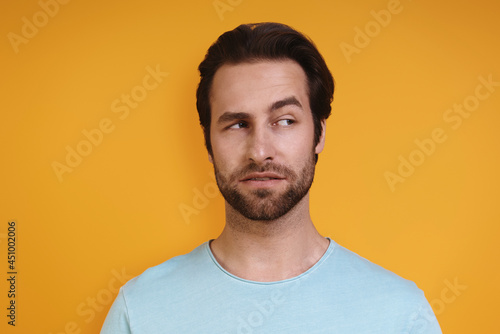 Portrait of young man in casual clothing looking uncertain while standing against yellow background © gstockstudio