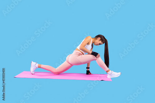 Girl with long ponytail in sports clothes and shoes practicing fitness exercises doing lunges forward on the pink mat.