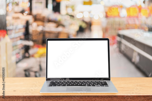 Empty screen laptop on a wooden table with abstract blurred image of supermarket store at the mall photo