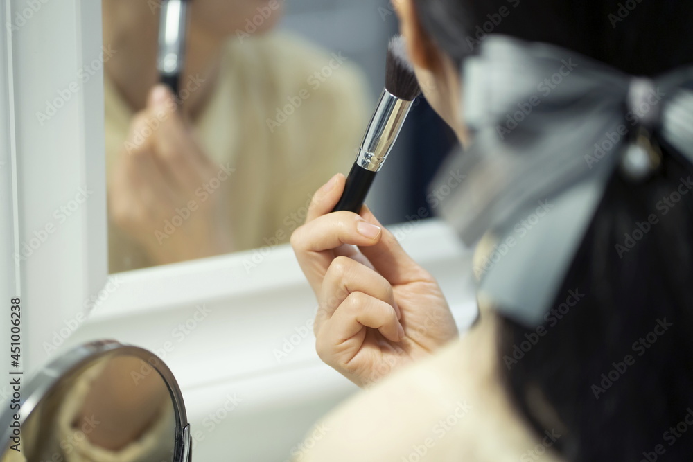 Woman applying make-up in mirror, using brush, close-up Woman applying make-up in mirror, using brush, close-up