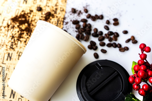 A cream colored plastic coffee mug and coffee beans lay on the table like a cup that fell and the coffee spilled out.