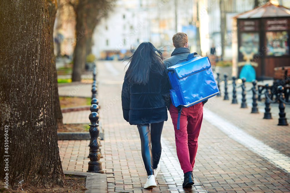 Deliveryboy walking with blue thermal bag on city street with young woman. Man of delivery service in hurry to deliver an order. Delivery service goes to give the order quickly to the client at night