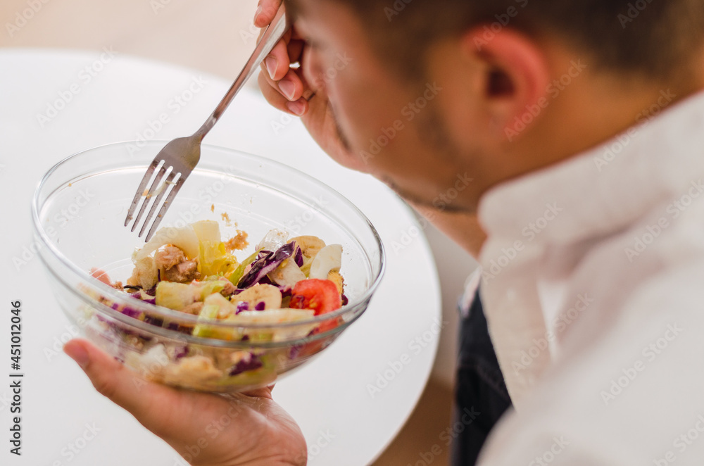 Close-up of young handsome Chinese man eating a fresh, delicious and healthy tomate salad with tune on the sofa in the living room of a minimalist and clean home Close-up of young handsome Chinese man eating a fresh, delicious and healthy tomate salad with tune on the sofa in the living room of a minimalist and clean home