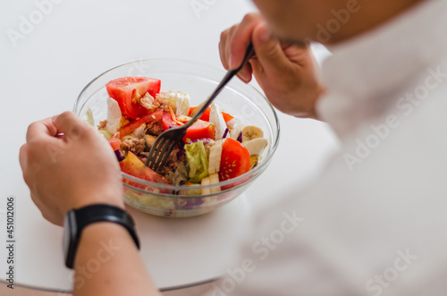 Close-up of young handsome Chinese man eating a fresh  delicious and healthy tomate salad with tune on the sofa in the living room of a minimalist and clean home