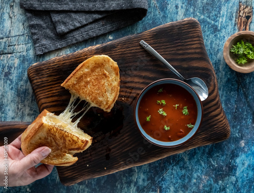 Quadro su tela Hand taking one half of a grilled cheese sandwich and a bowl of tomato soup