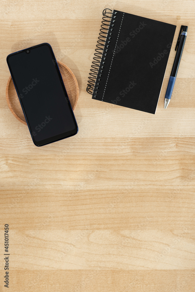 Smart phone, notebook and pen in black color, on wood background. Office banner style. Smart phone, notebook and pen in black color, on wood background. Office banner style.